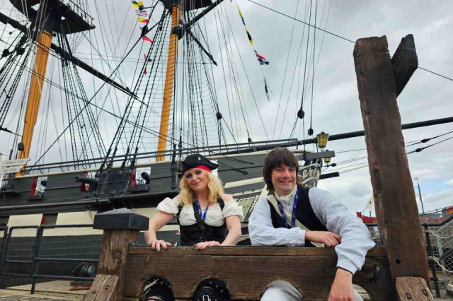 Two costume interpreters sit in the stocks in front of HMS Trincomalee in Hartlepool