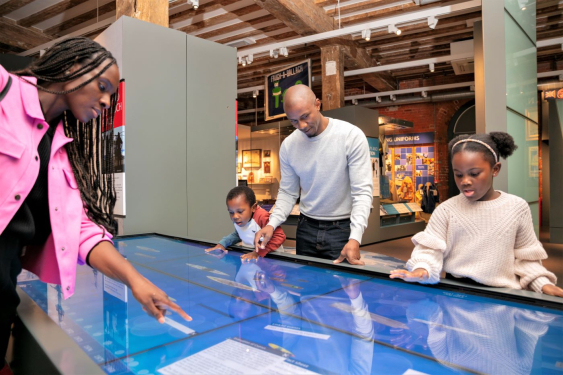 Family (mother, father, and two children) using a large touch screen display at the National Museum of the Royal Navy