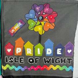 Spray painted quilt for Ilse of Wight Pride. There is a rainbow pinwheel in the centre and small beach huts spell pride