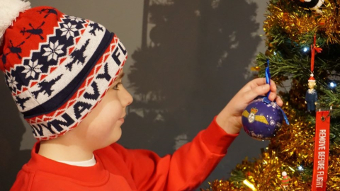 Child placing a bauble on a christmas tree