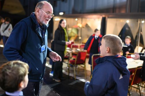 An elderly male volunteer talks to children at the Fleet Air Arm Museum