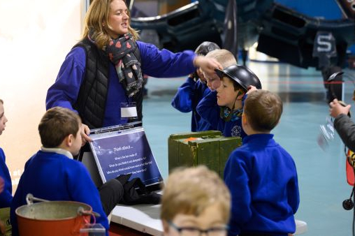 Children gather round their teacher as she talks to them at the Fleet Air Arm Museum