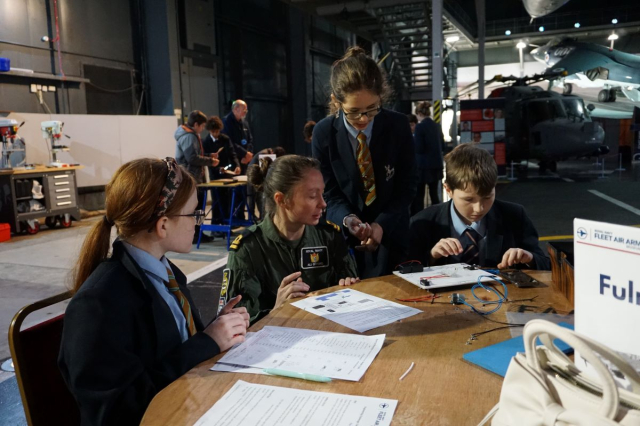 A servicewoman talks to a group of primary age children at the Fleet Air Arm Museum