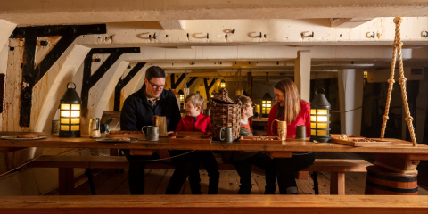 Family sit at a mess table inside HMS Trincomalee, an 18th century tail sail wooden ship of the Royal Navy. 
