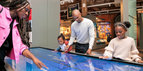 Family (mother, father, and two children) using a large touch screen display at the National Museum of the Royal Navy