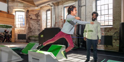 Young girl uses the obstacle course at Action Stations as her father watches. 