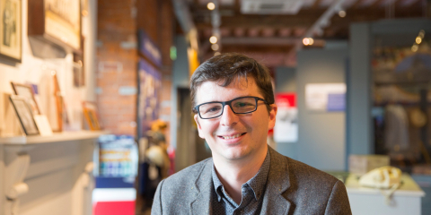 A person smiles facing the camera with a museum gallery in the background.