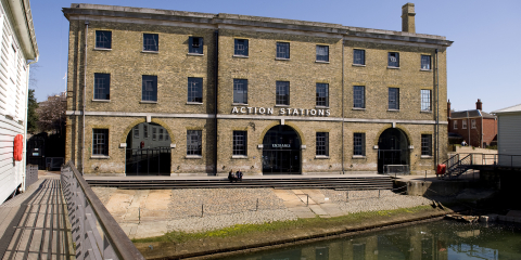 The front of a large historic building with a sign that says 'Action Stations'